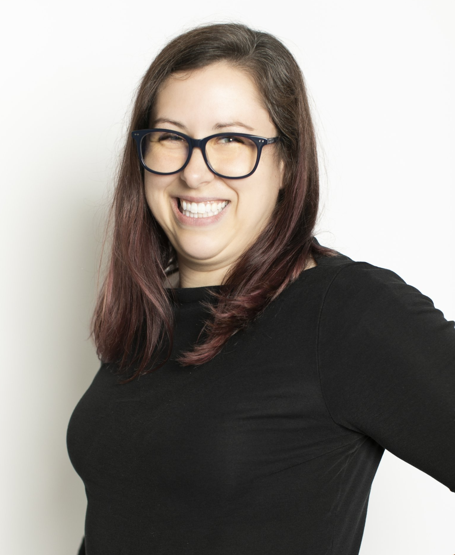 Smiling woman with black glasses and dark hair, wearing a black top against a white background