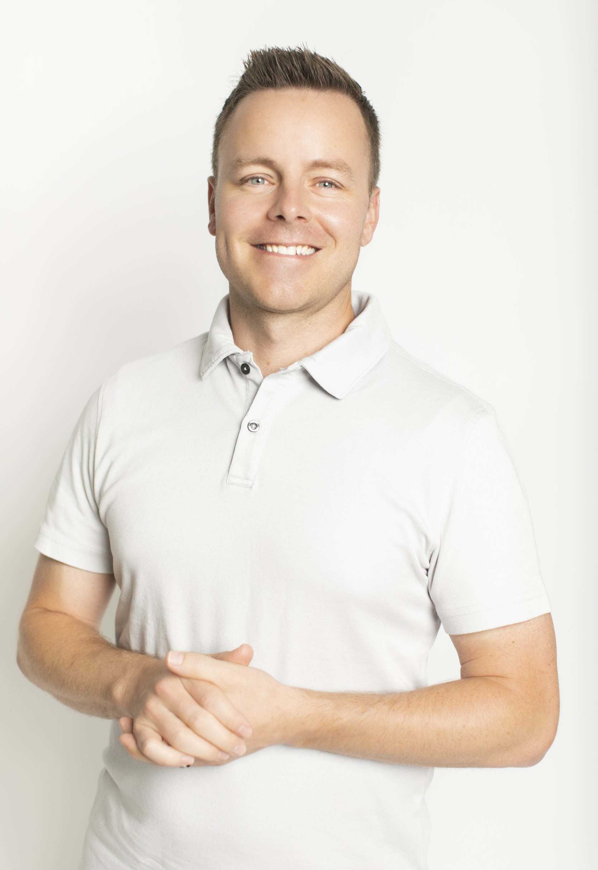 Smiling person in a white polo shirt standing with hands clasped against a light background