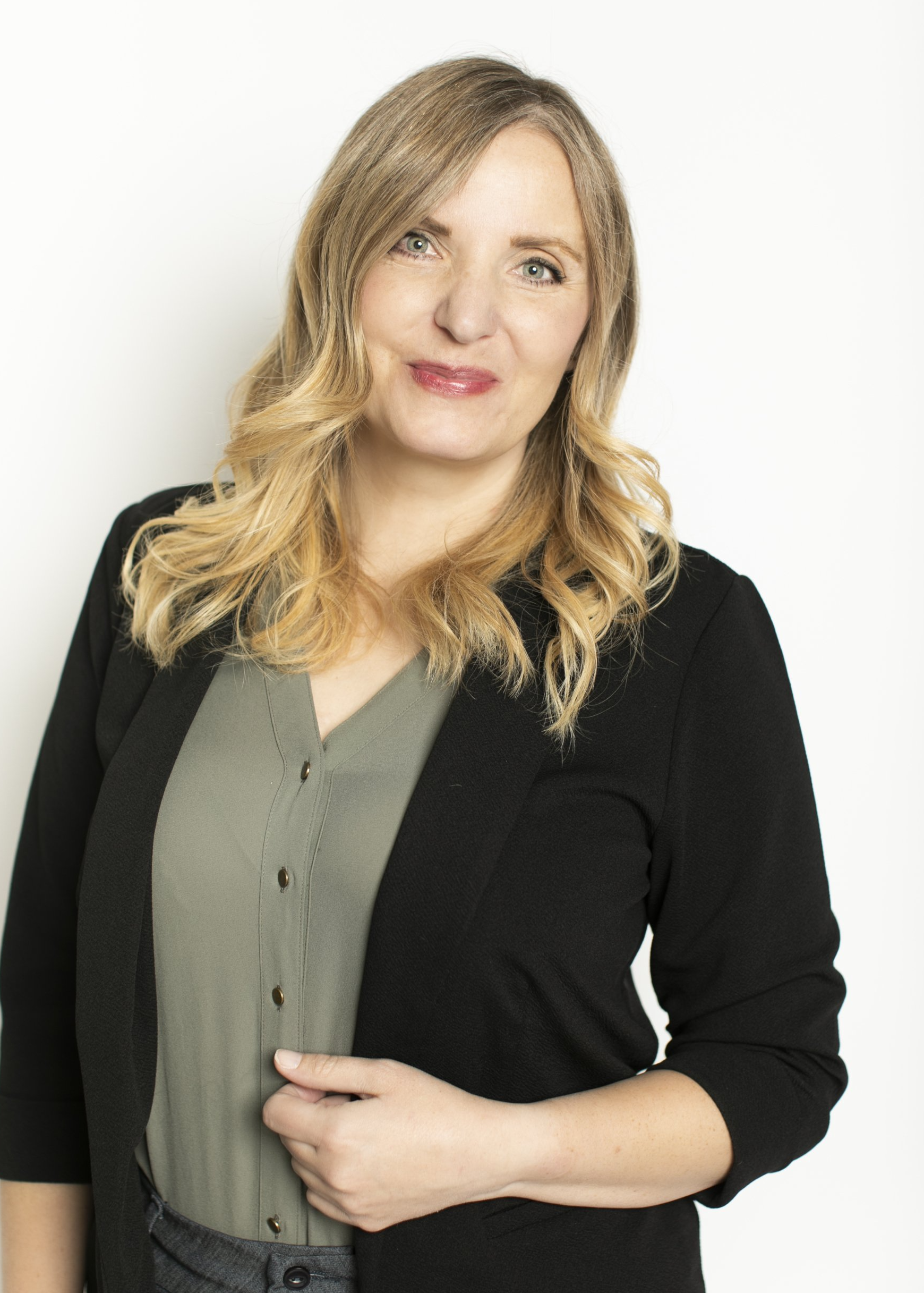 Portrait of a woman in a black cardigan over an olive blouse, standing against a white background.