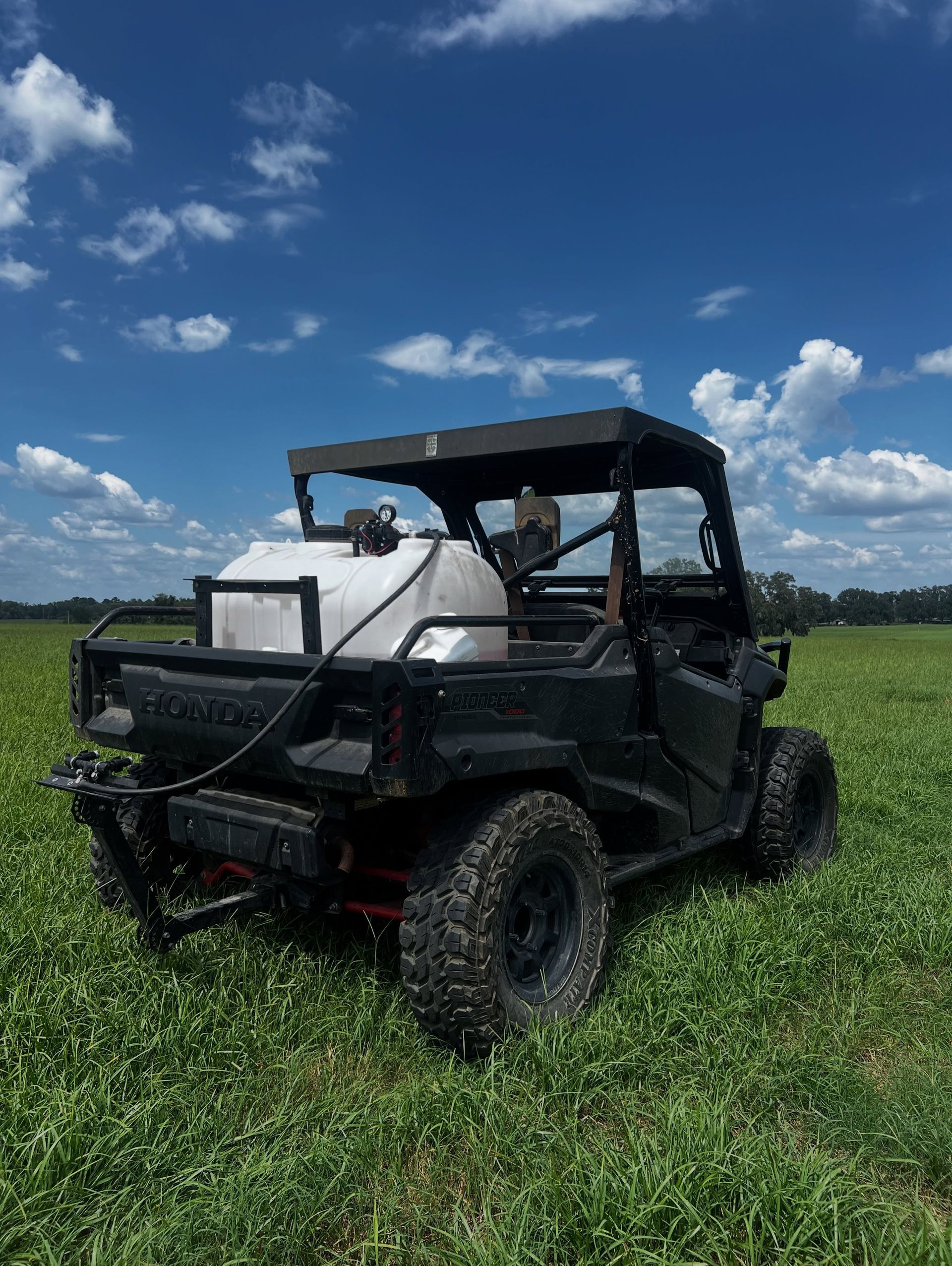 Black utility vehicle parked in a green field under a blue, cloudy sky