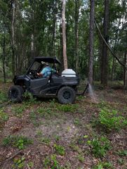 Person driving a black side-by-side ATV in a wooded area
