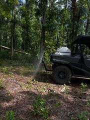 ATV parked in a wooded area with water spraying nearby and a white cooler on the back
