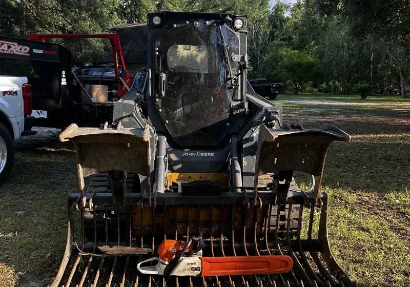 Front view of a skid steer with a brush grapple attachment in a muddy field