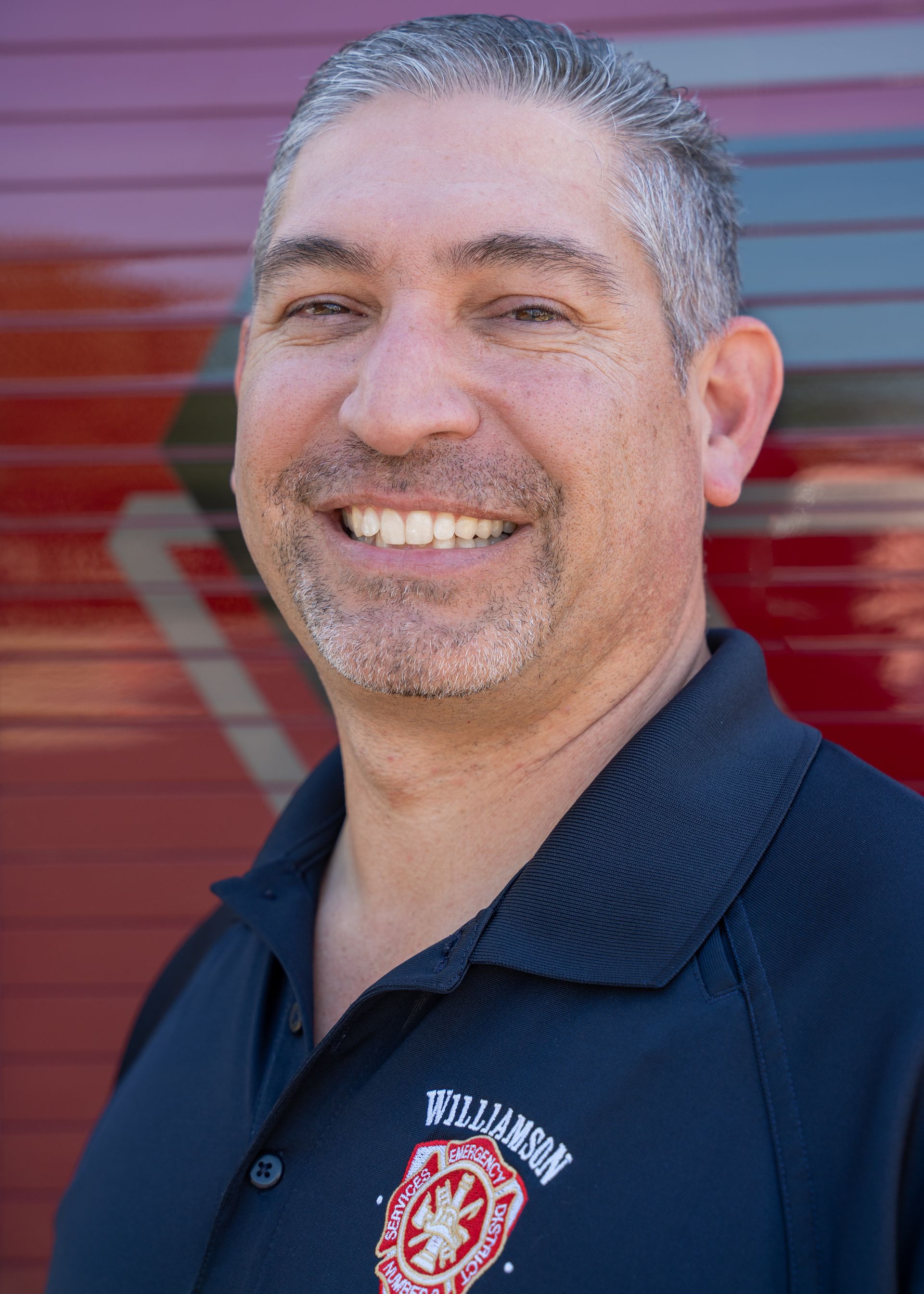 A man in a black shirt is smiling in front of a red wall.