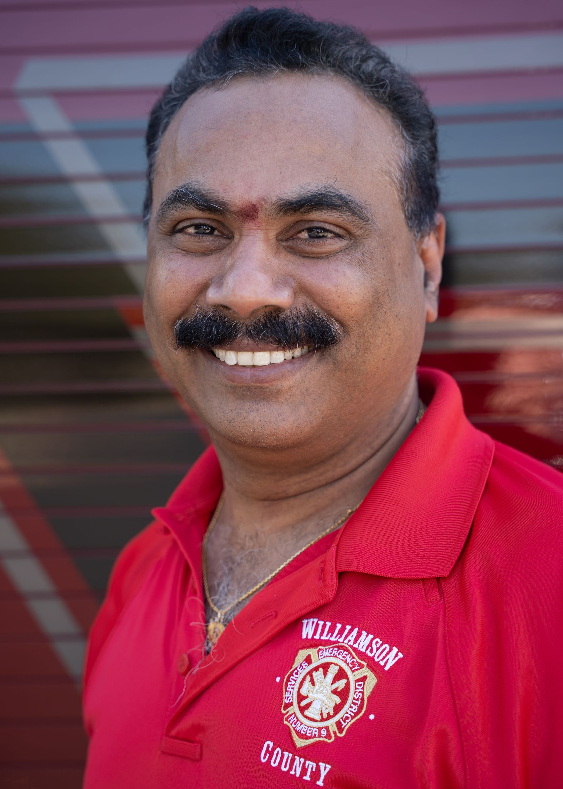 A man with a mustache is wearing a red shirt that says Williamson county