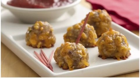 A white plate topped with sausage balls next to a bowl of dipping sauce.