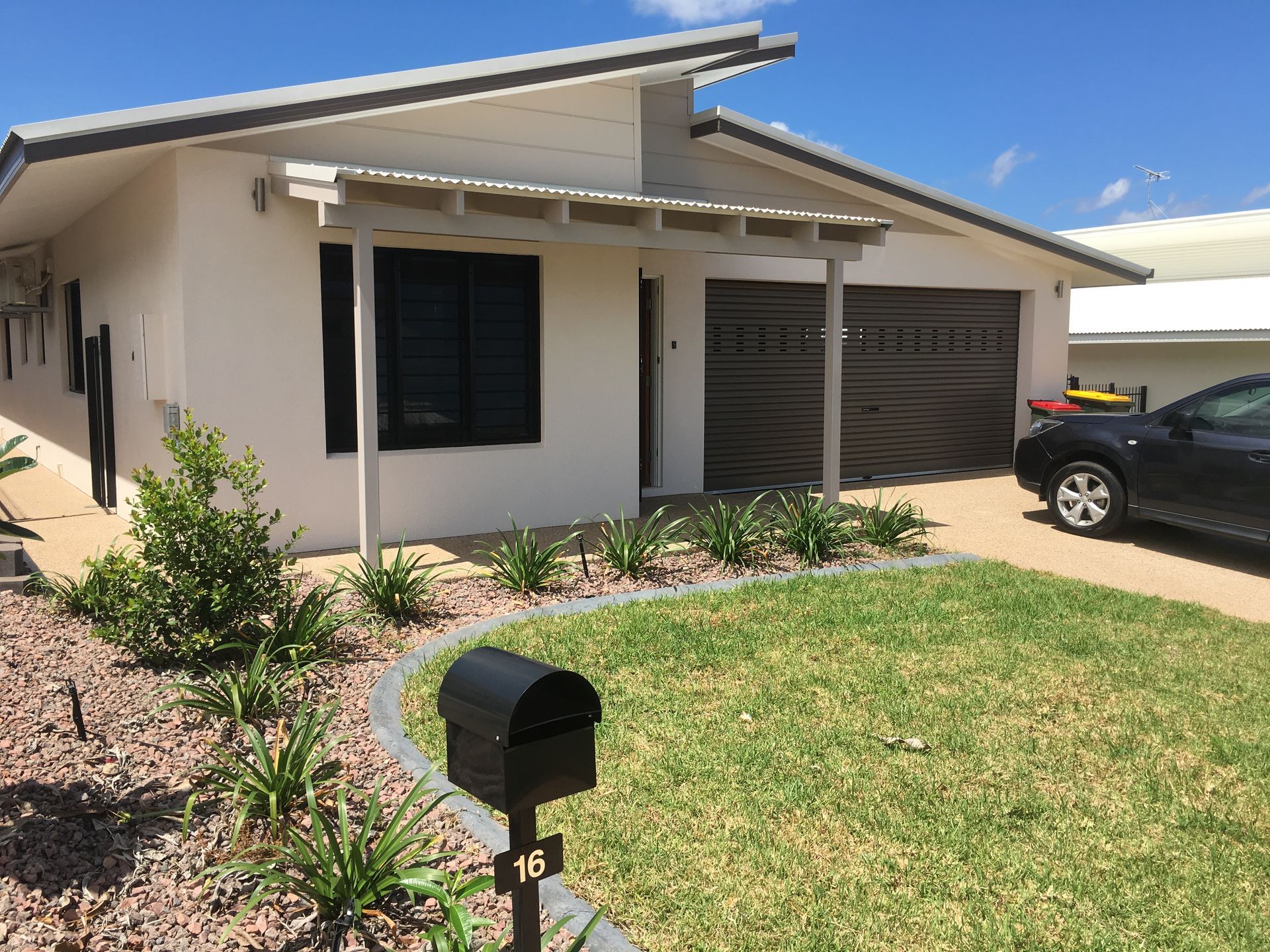 White house with grey trim, brown garage doors, and green lawn. A black car is parked nearby — AKW Builders Pty Ltd In Leanyer, NT
