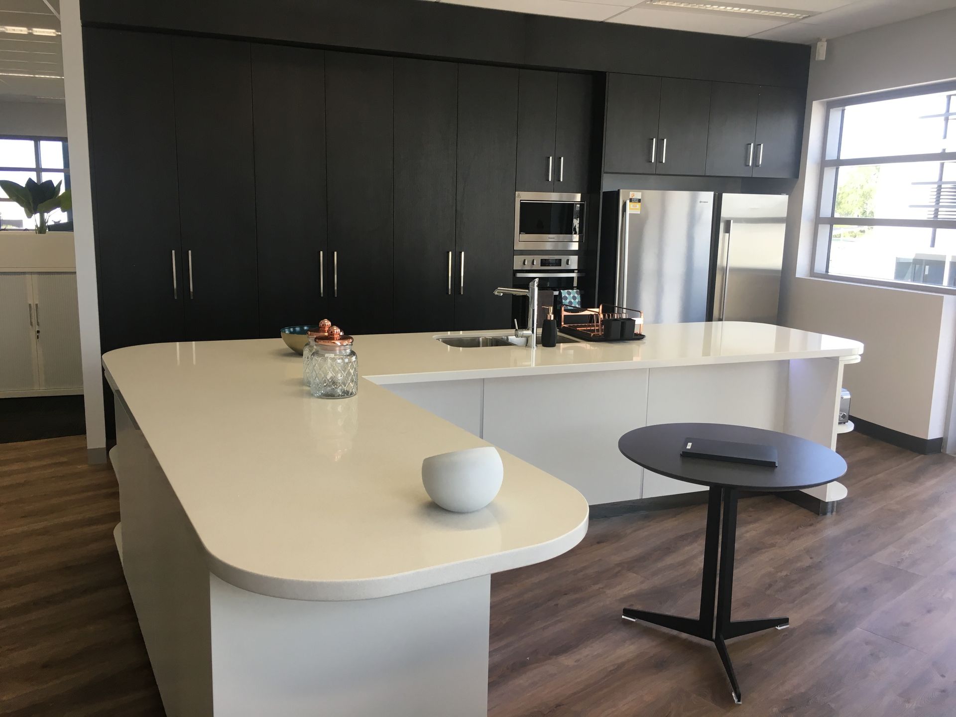 Modern kitchen with white island, black cabinets, stainless steel appliances, and a small table — AKW Builders Pty Ltd In Leanyer, NT