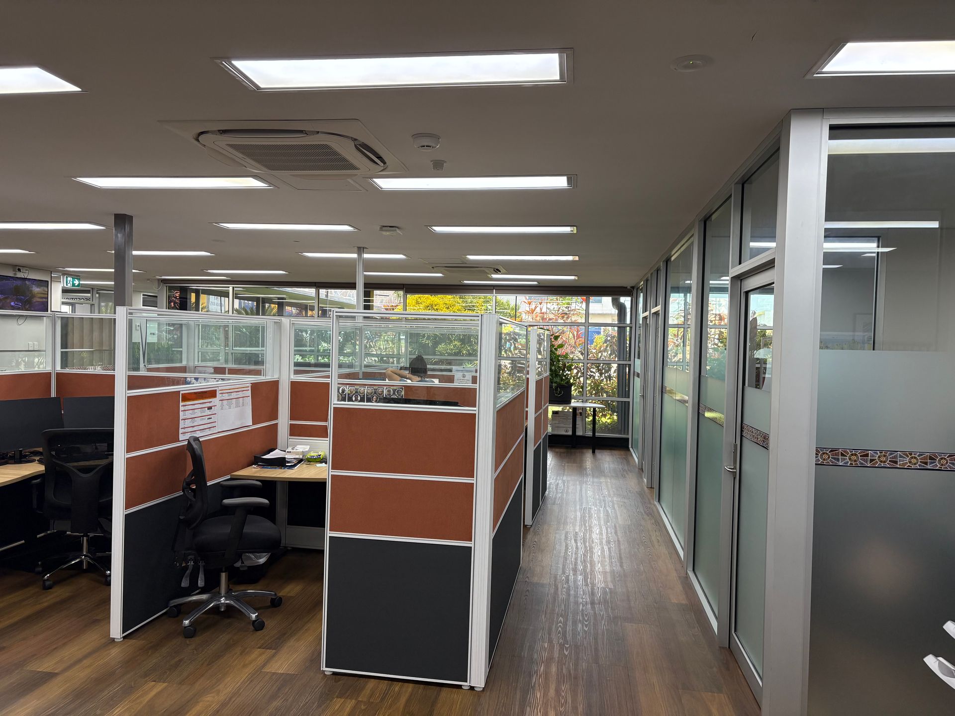 Office cubicles and glass-walled rooms in a well-lit interior. Brown and grey dividers, wooden floor, windows — AKW Builders Pty Ltd In Leanyer, NT