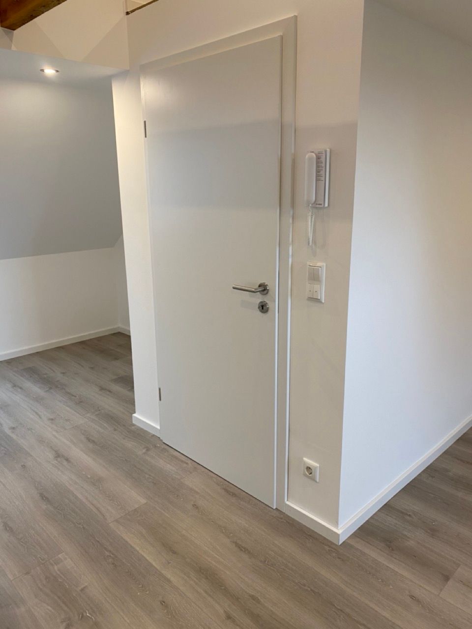 Leeres, modernes Zimmer mit weißer Tür, hellem Holzboden und grauer Akzentwand