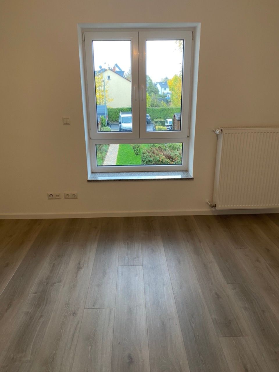 Leeres Zimmer mit Holzboden, einem Fenster und einem weißen Heizkörper