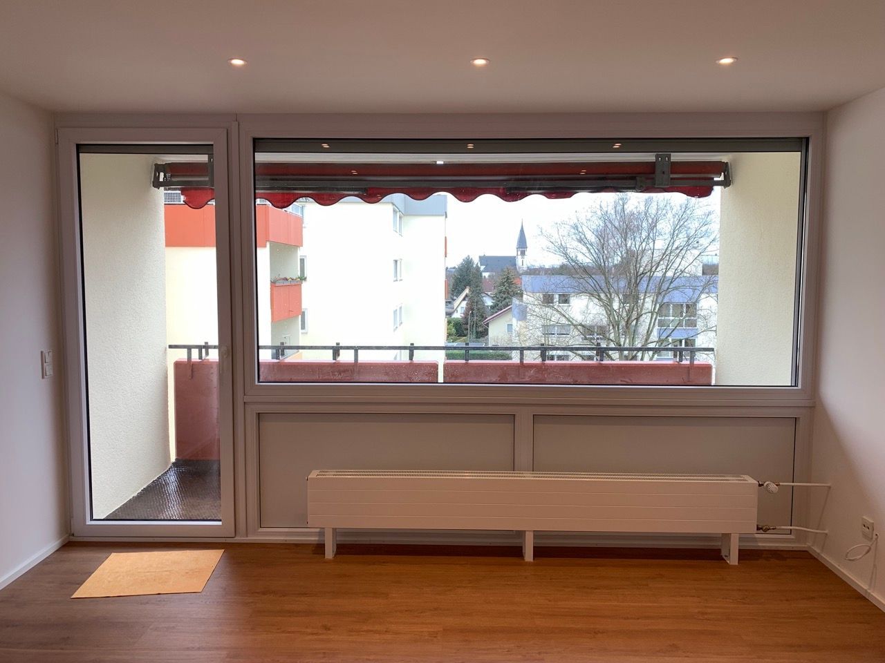 Minimalistisches Zimmer mit großem Fenster, Schiebetür, weißer Bank und Holzboden.