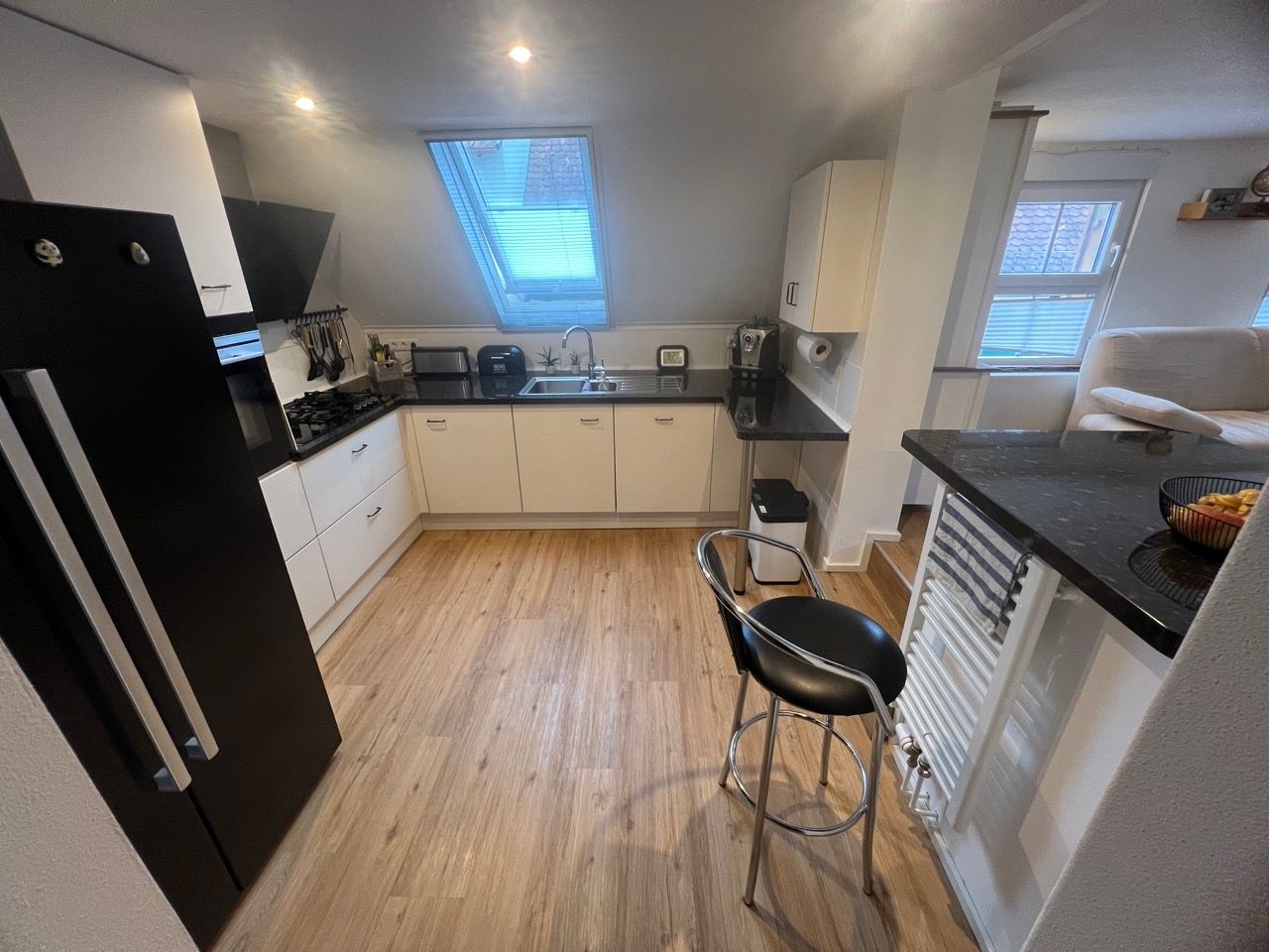 Helle Küche mit schwarzem Kühlschrank, weißen Schränken, Dachfenster und Frühstücksbarhocker