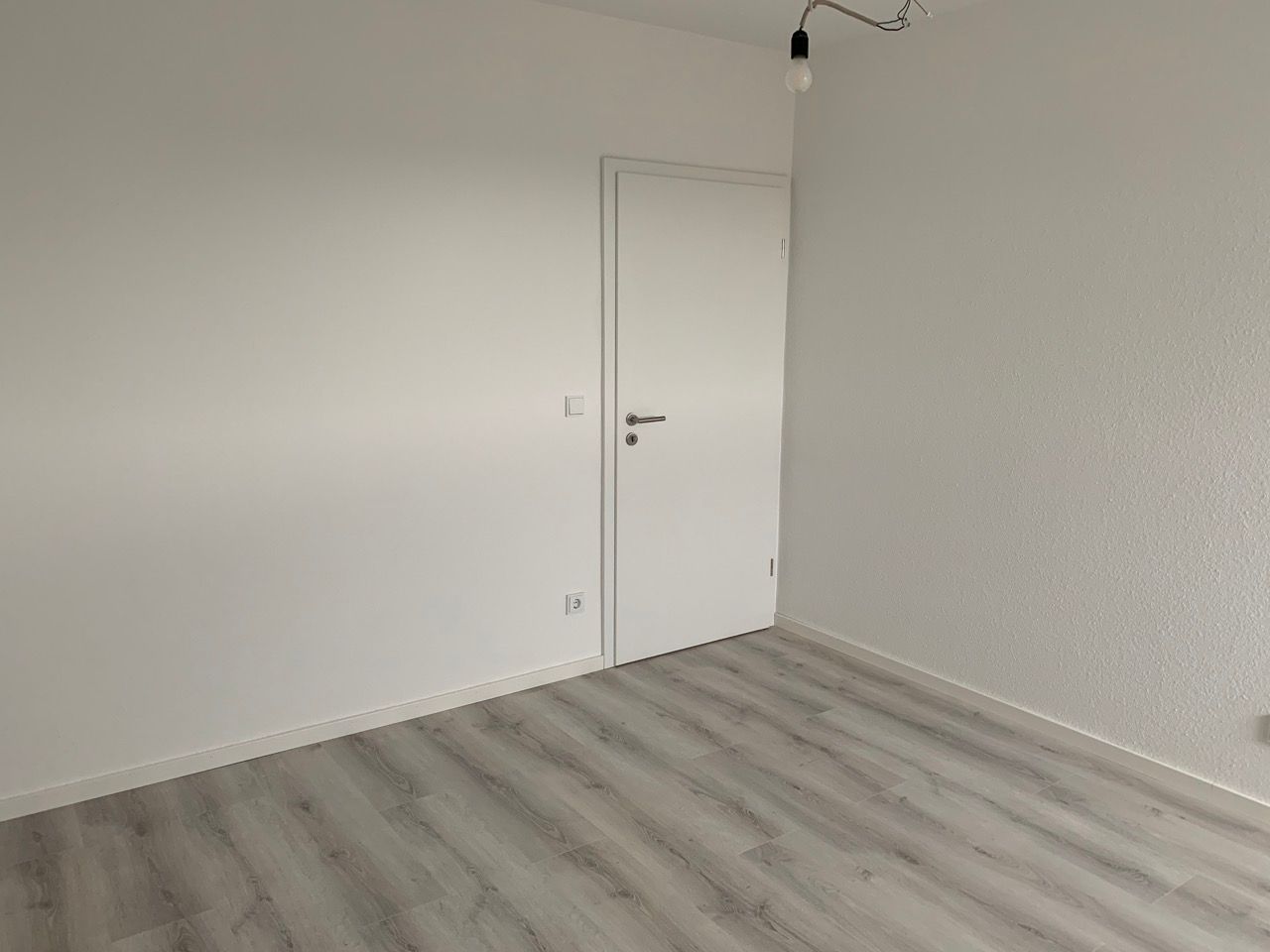 Leerer weißer Raum mit hellgrauem Holzboden und einer geschlossenen weißen Tür