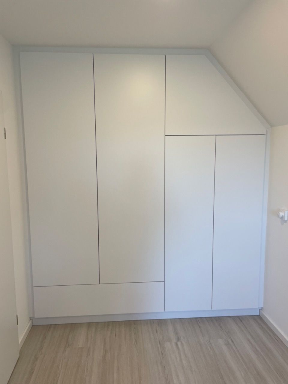 Weiße Einbauschränke in einem kleinen Zimmer mit Dachschräge und hellem Holzboden