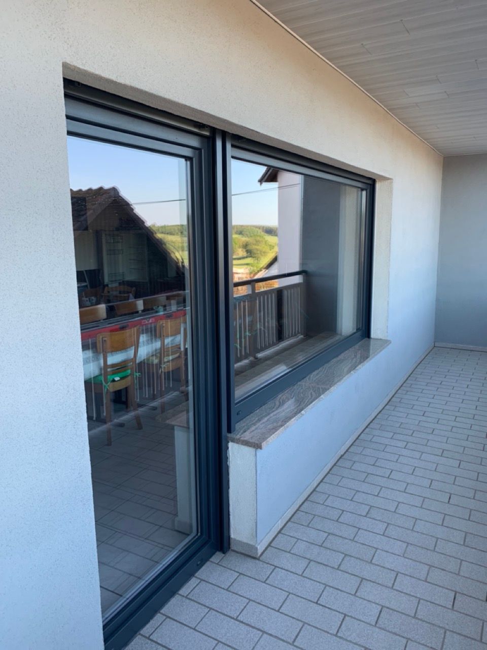 Balkon mit großen Glasschiebetüren, weißen Wänden und Fliesenboden mit Blick auf die umliegenden Häuser.
