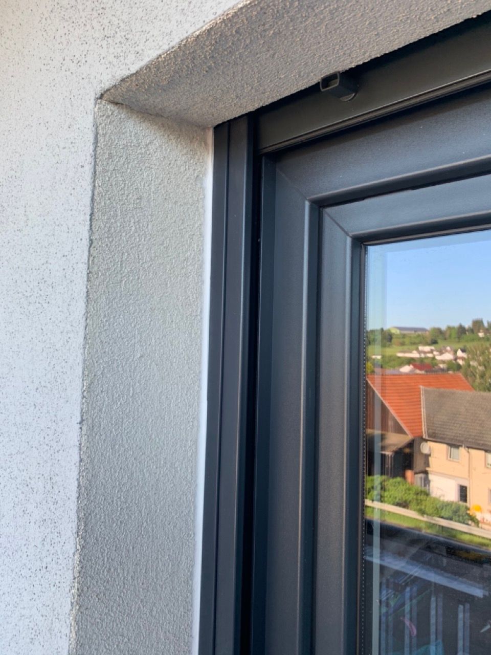 Nahaufnahme eines Fensterrahmens und einer Fensterbank, in deren Glas sich das Stadtbild spiegelt.