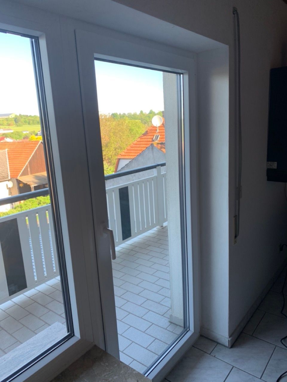 Innenblick durch offene Balkontüren auf den gefliesten Balkon und die Dächer draußen