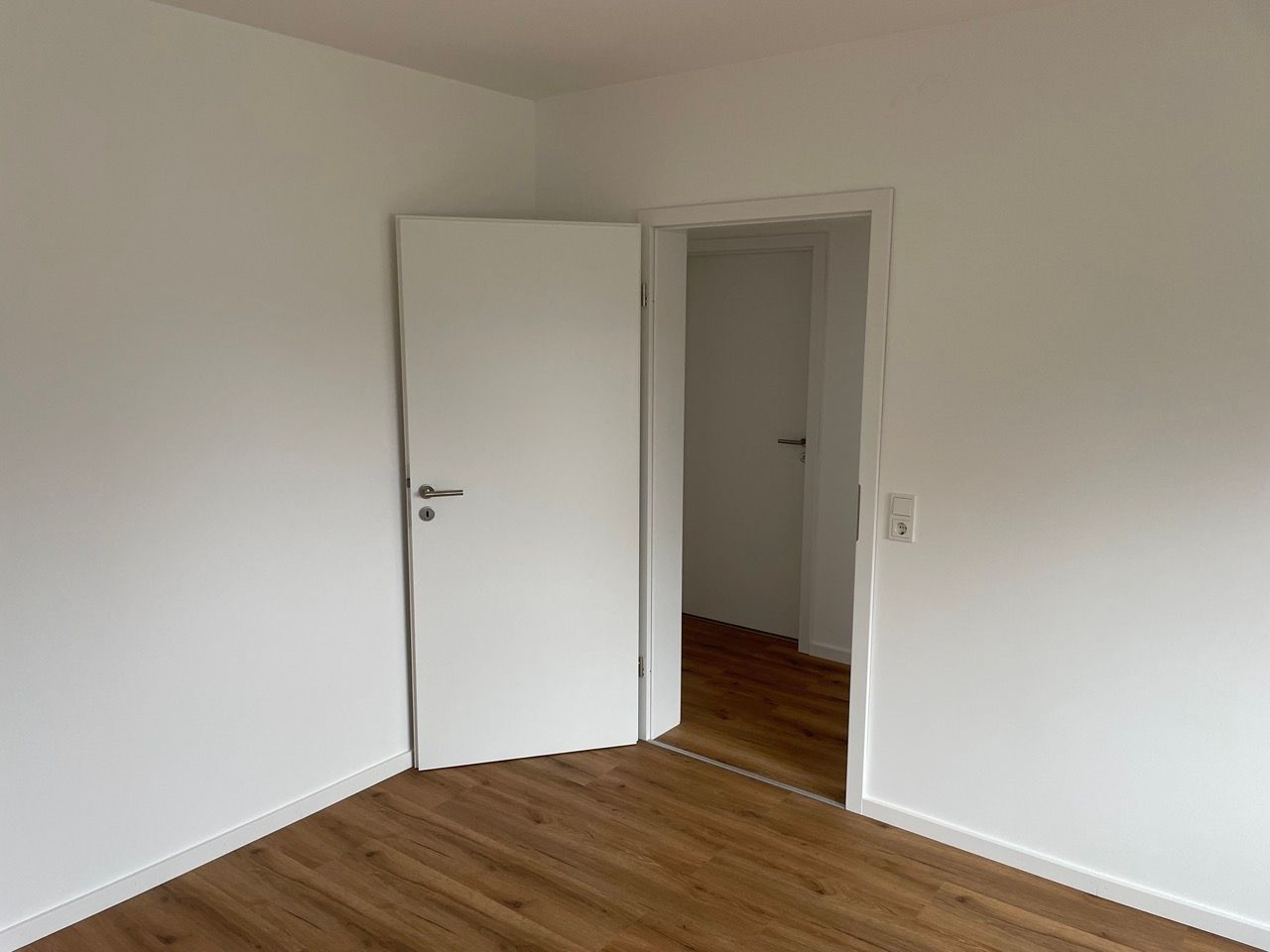 Leerer weißer Raum mit offener Tür und Holzboden