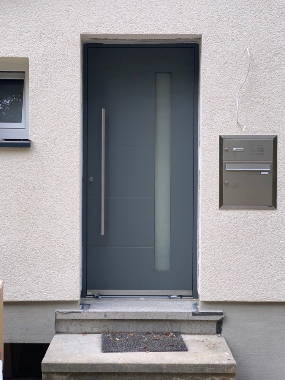 Moderne Haustür mit Milchglasscheibe, Stufen und danebenliegendem, an der Wand montiertem Briefkasten