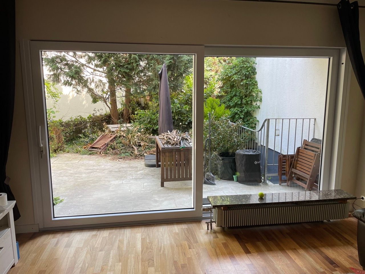 Wohnzimmer mit großer Glasschiebetür zur Terrasse und zum Garten, mit Stühlen und einem kleinen Tisch im Freien