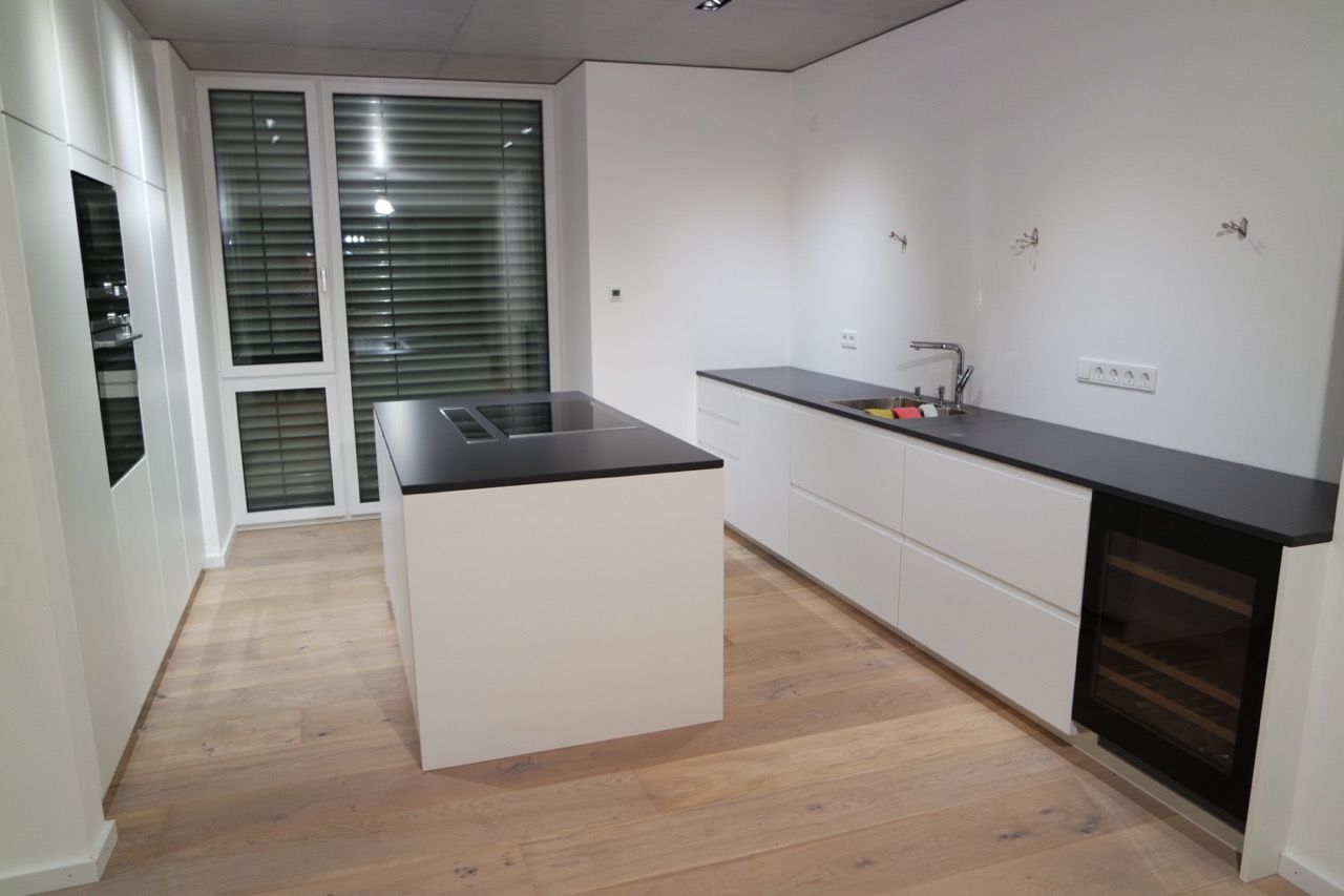 Moderne Küche mit weißen Schränken, dunklen Arbeitsplatten und einer zentralen Kochinsel, vom Eingang aus gesehen.