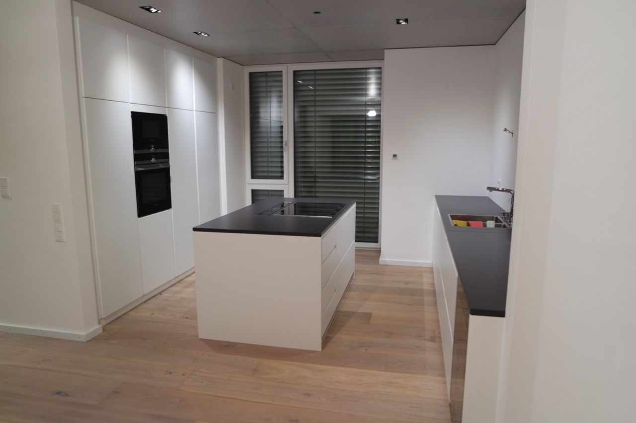 Moderne, leere Küche mit weißen Schränken, schwarzer Kücheninsel und Holzboden.