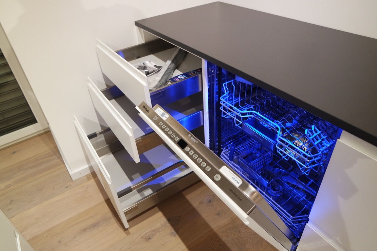 Weißer Schreibtisch mit offenen Schubladen und einem blau beleuchteten Computer-Tower in einem eleganten Schrank.