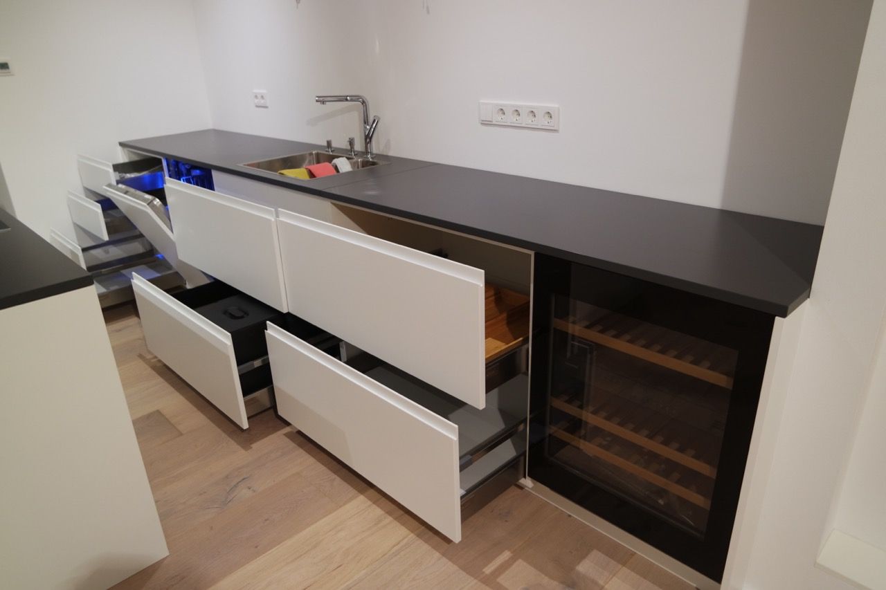 Moderne Küche mit offenen Schubladen und schwarzer Arbeitsplatte, die Spüle und Einbaubackofen zeigt.