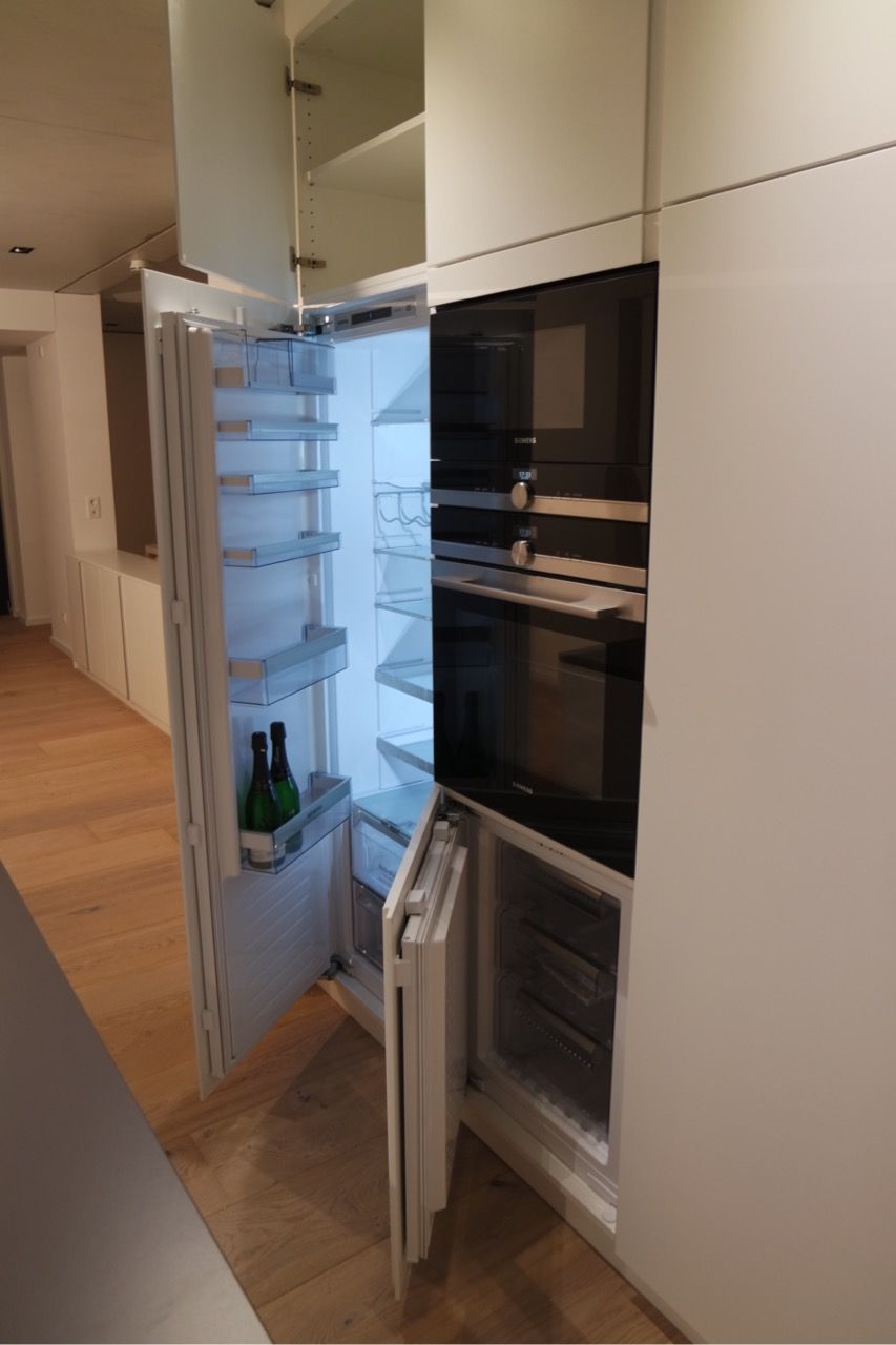 Offener Einbauküchenschrank mit Regalen und Mikrowelle in einer modernen weißen Küche.