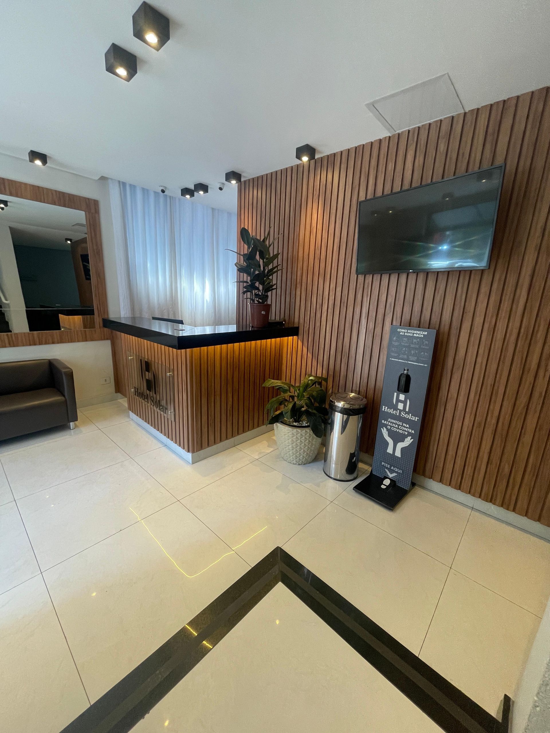 Um lobby de hotel com um sofá e uma tv na parede - Hotel Solar Bela Vista