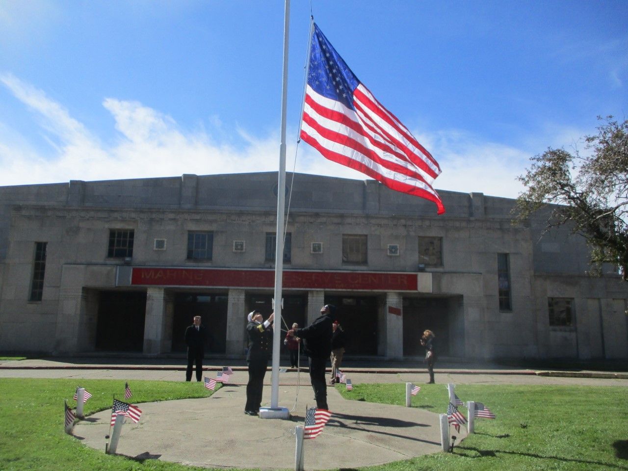 U.S. flag flying in front of a gray stone building with a few people standing at the entrance.