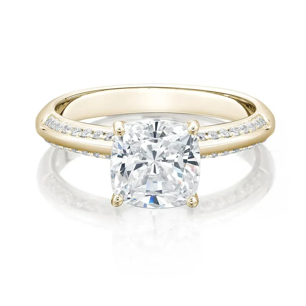 Yellow gold engagement ring with a cushion-cut diamond center stone and diamond-studded band.