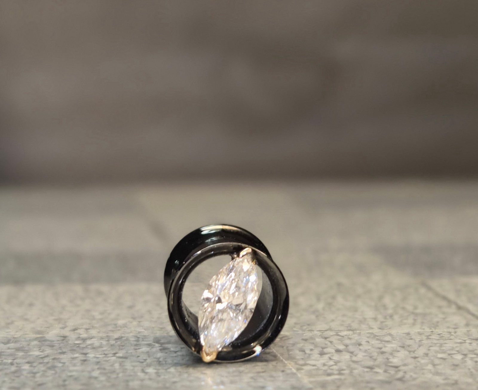 Black ear gauge with a large, marquise-cut, clear jewel centered within the opening.
