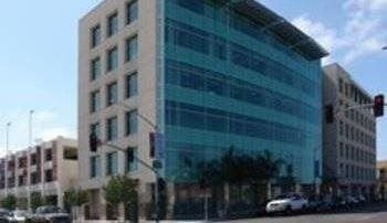 Modern office building with glass facade, blue-green hue, and surrounding street with cars.