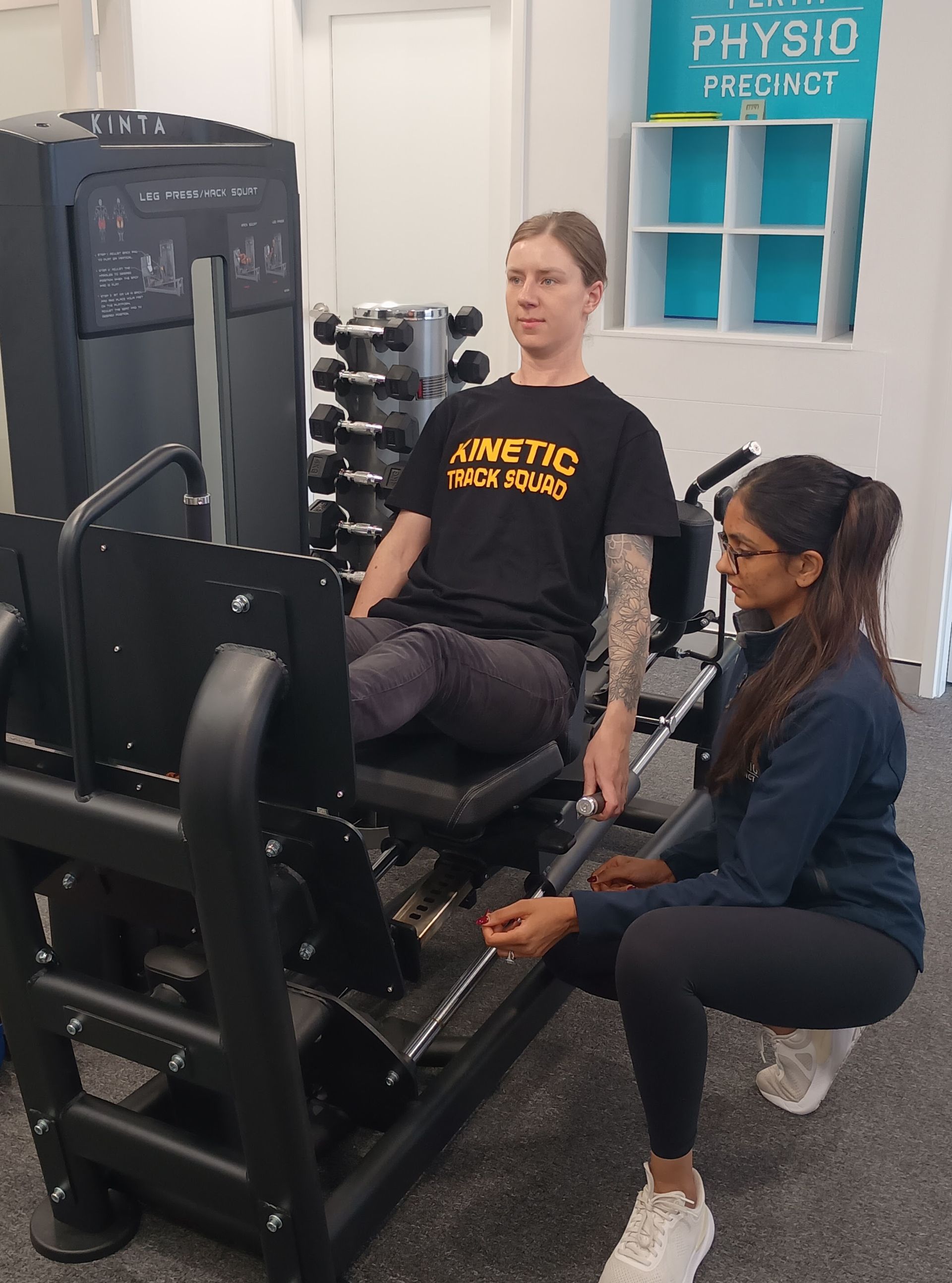 A person performs a single-arm dumbbell overhead press while seated on a weight bench in a gym.