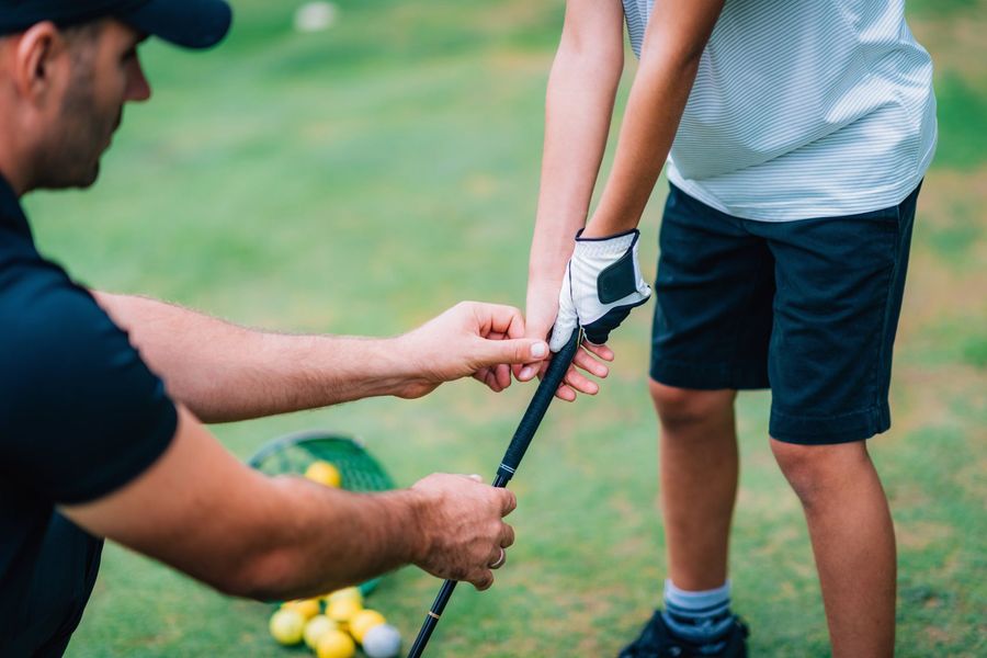 Golfer helping a child hold a golf club on a green course