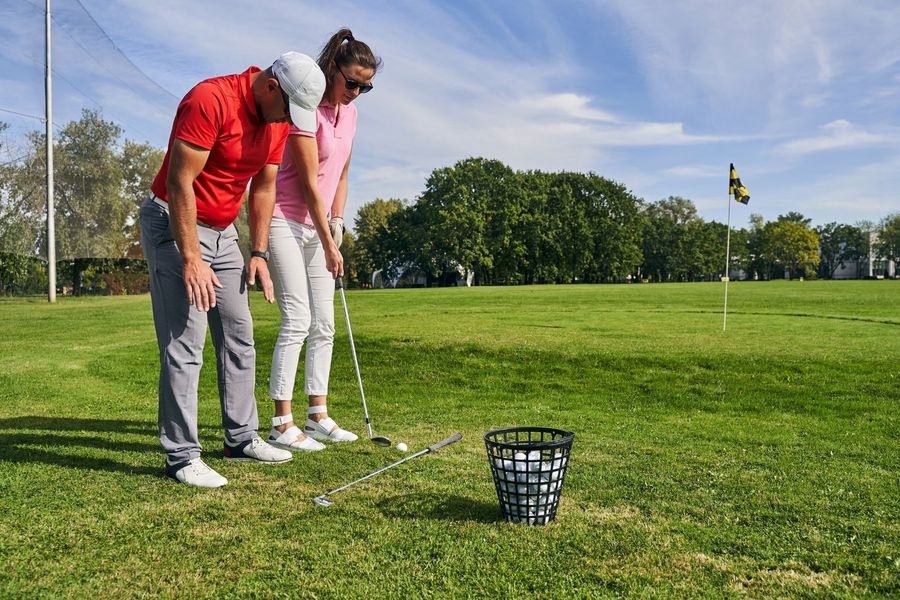 Two golfers practicing putting on a green beside a ball basket and flagstick