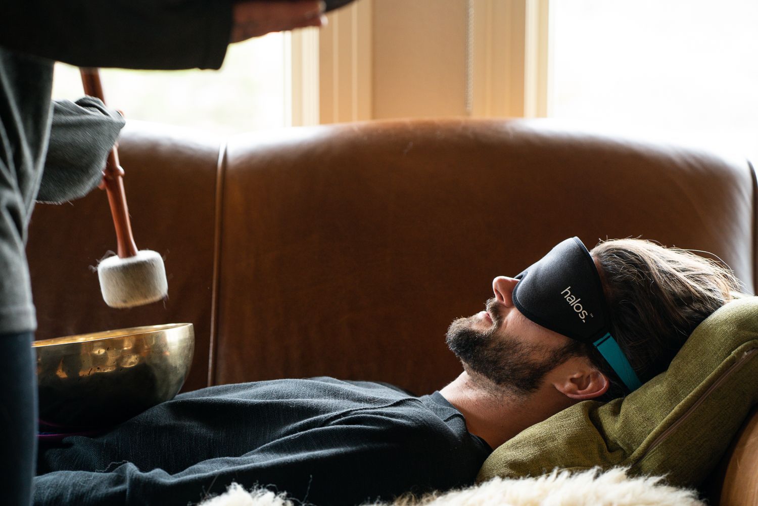 Man with eye mask reclines during sound bowl meditation; indoor setting.