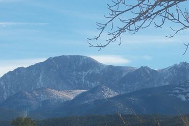 Snow-dusted mountain ridge beneath a clear blue sky, with bare branches in the foreground at Bodhi's Academy in Colorado
