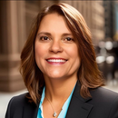 Woman with brown hair smiles in a suit, downtown setting.
