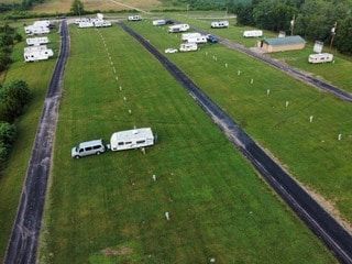 Aerial view of an RV park featuring multiple trailers and vehicles parked along several paved driveways on a grassy lot.