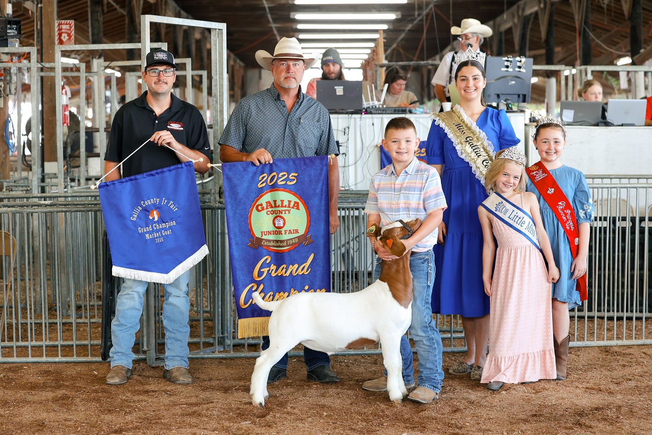 A judge shakes hands with a youth showing a pig in an arena at a livestock competition, surrounded by spectators.