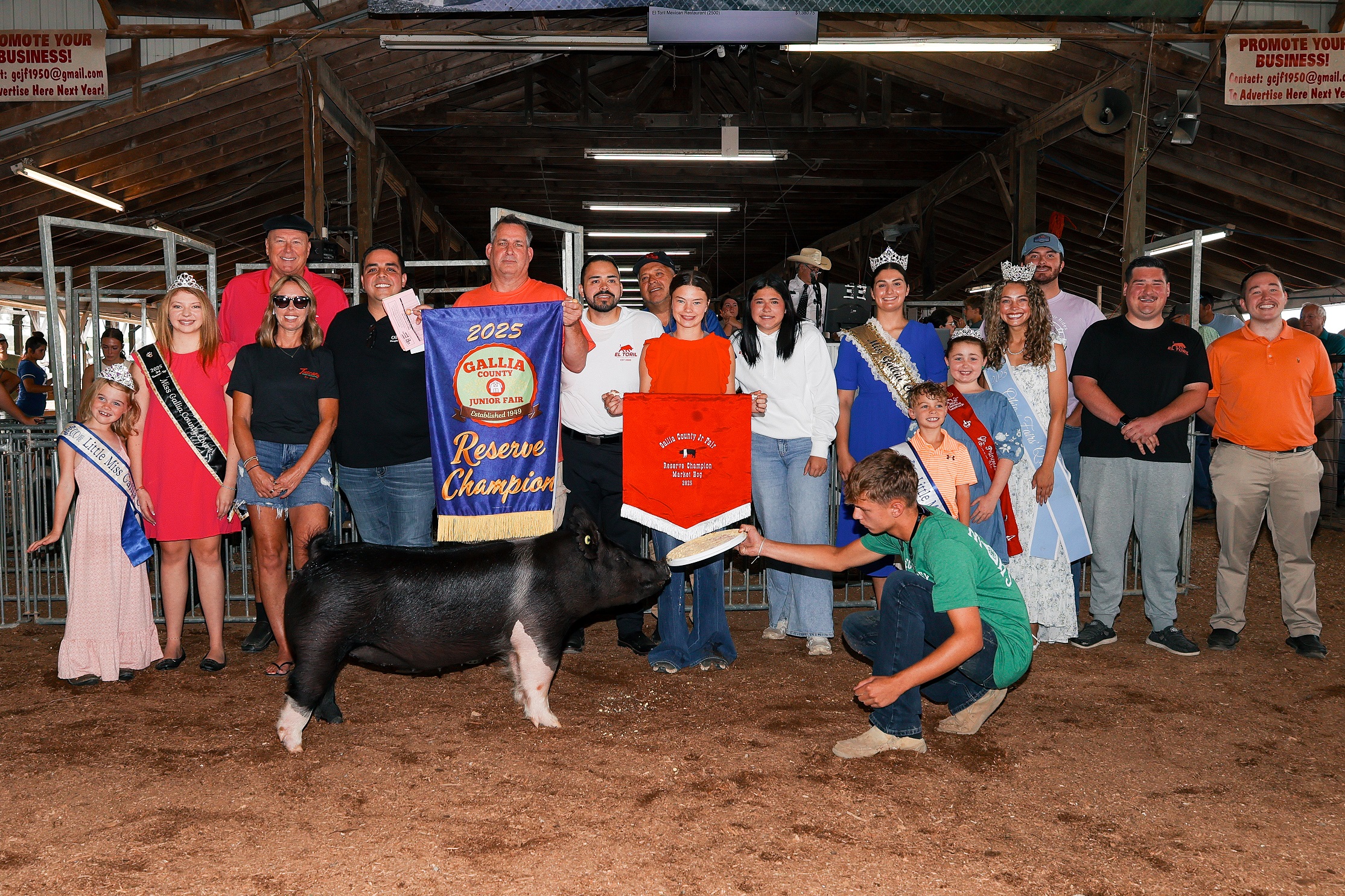 Participants in a livestock competition stand in a ring with goats, while an instructor observes them.