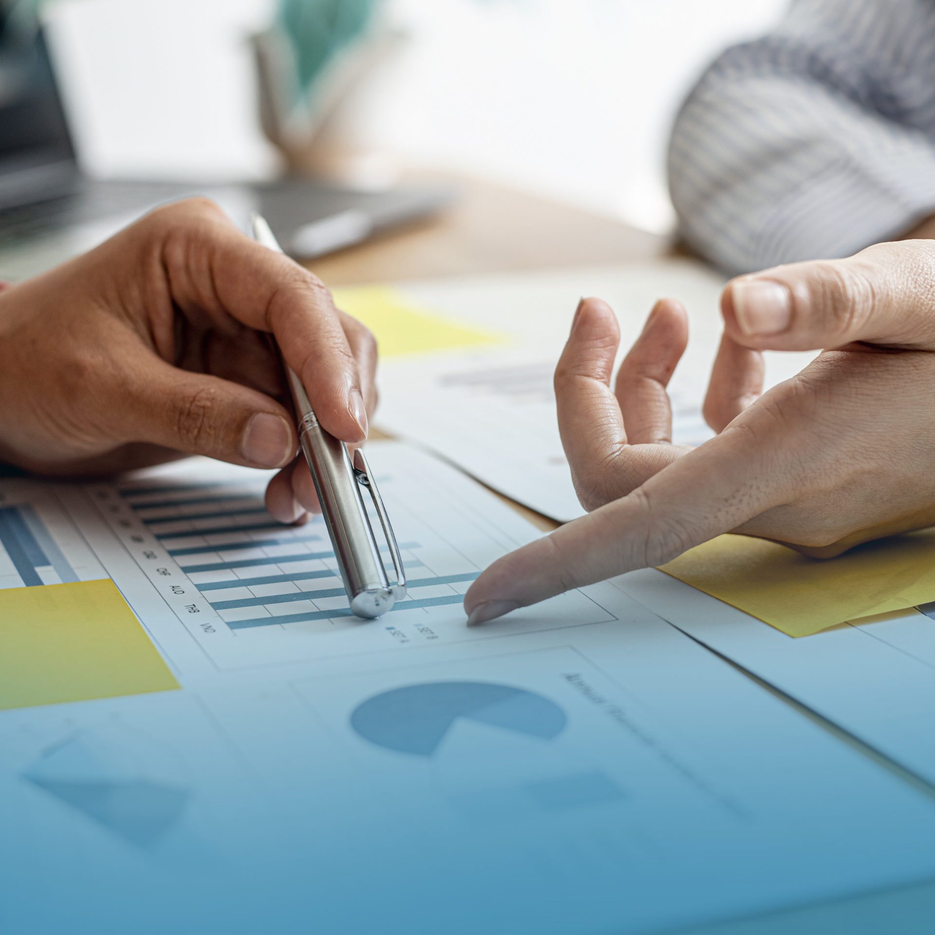 Hands pointing at a blue financial chart with documents on a desk