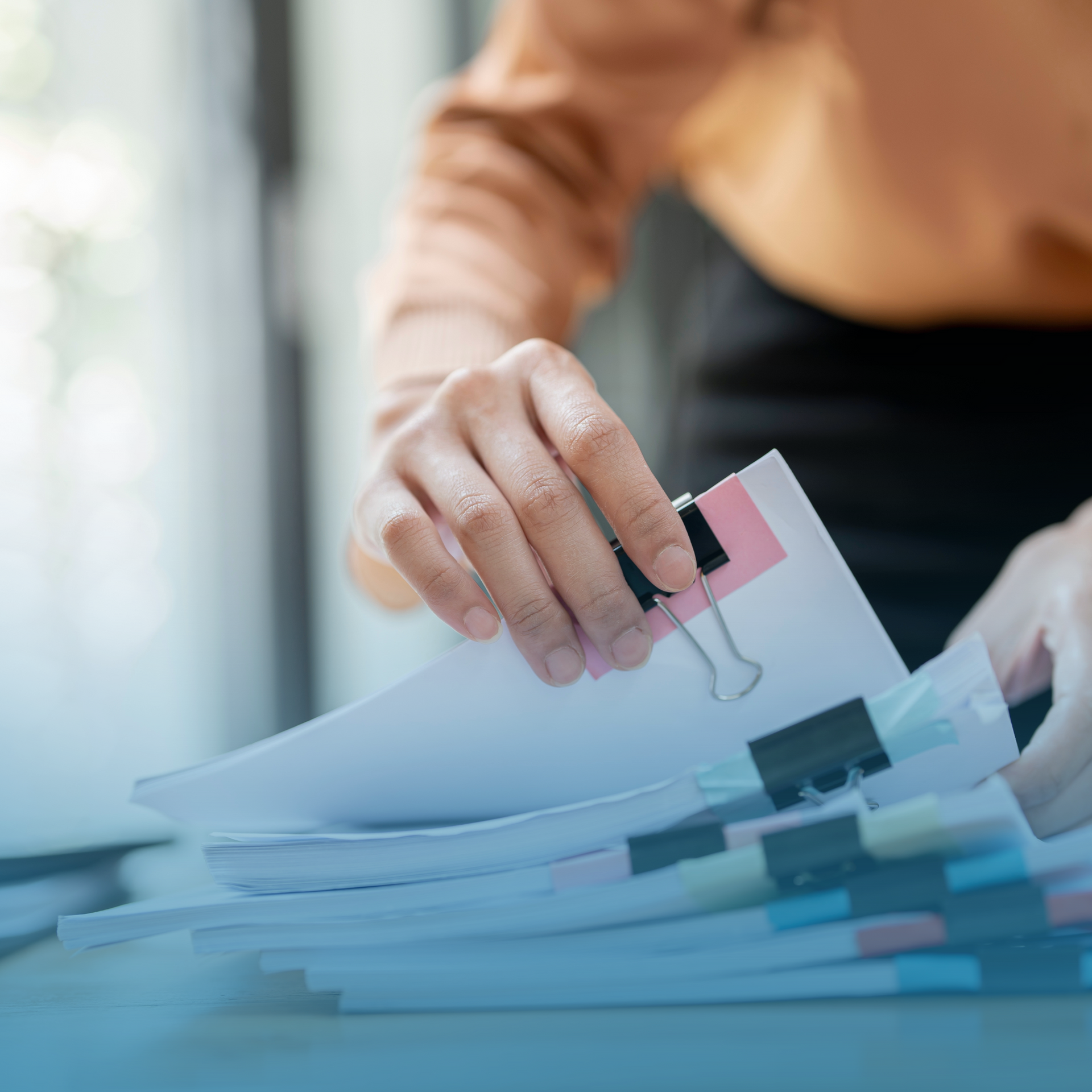 Hand placing a pink clip on a stack of papers at a desk