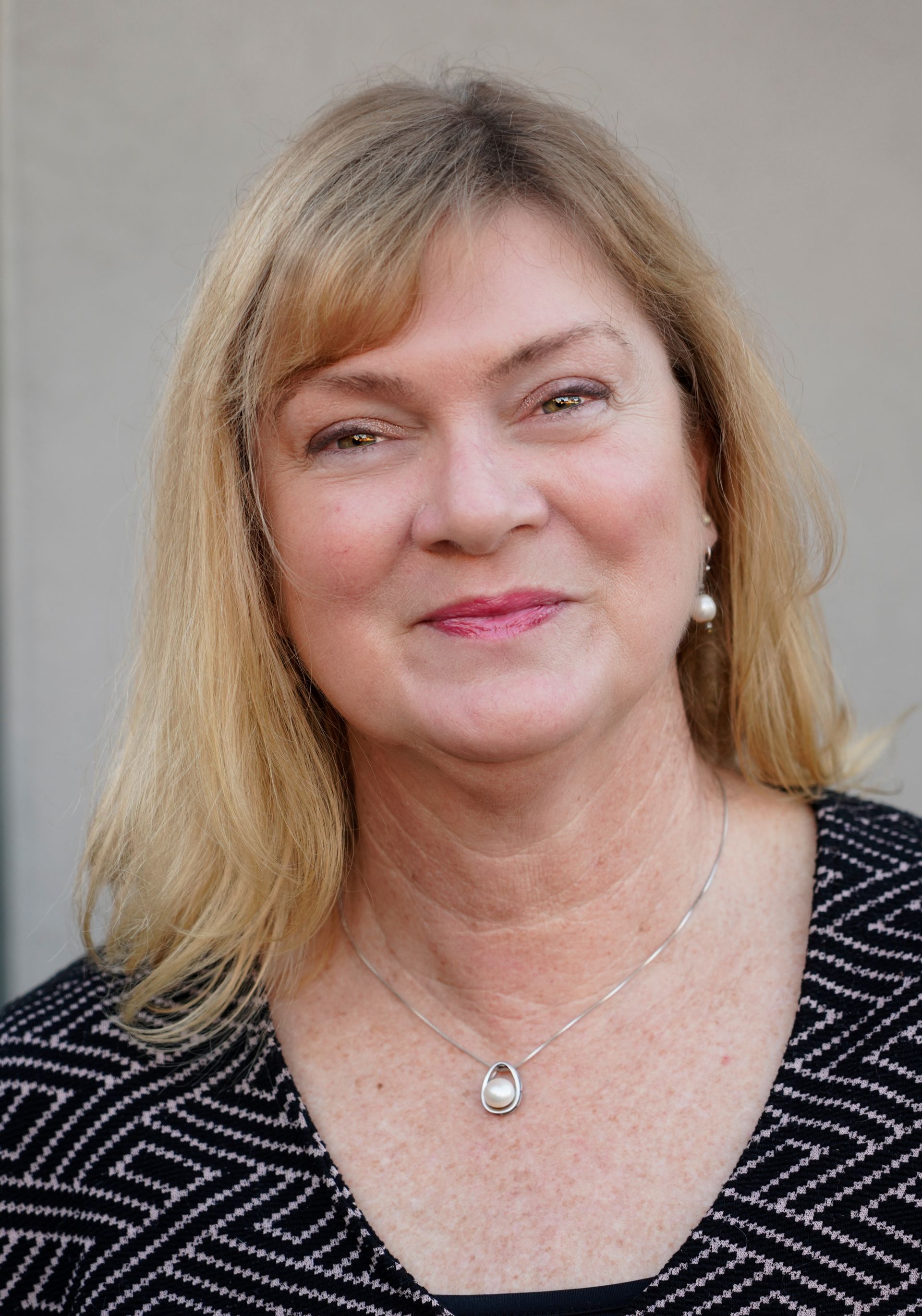 Portrait of a smiling woman with blonde hair wearing a black patterned top and necklace
