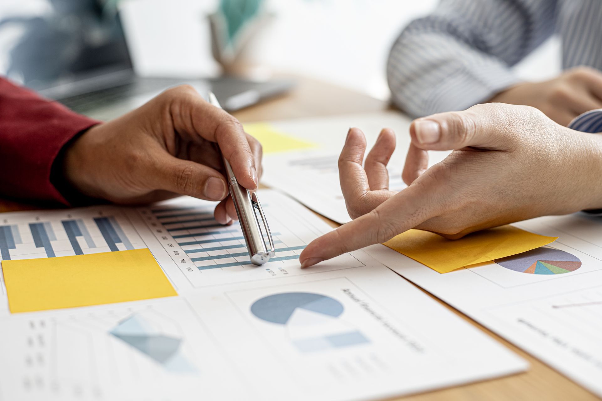Hands reviewing printed charts and graphs at a meeting table with a pen and tablet