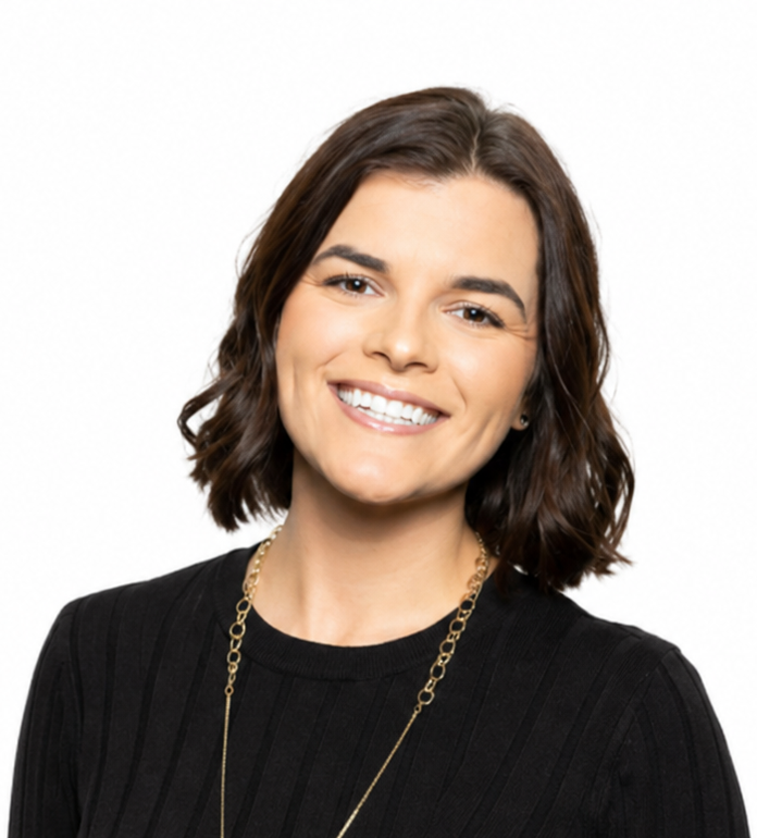 Smiling person with short dark hair wearing a black top and gold necklace against a white background