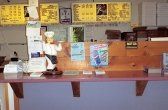 Counter in a restaurant with menu boards, a chef figurine, and order window.